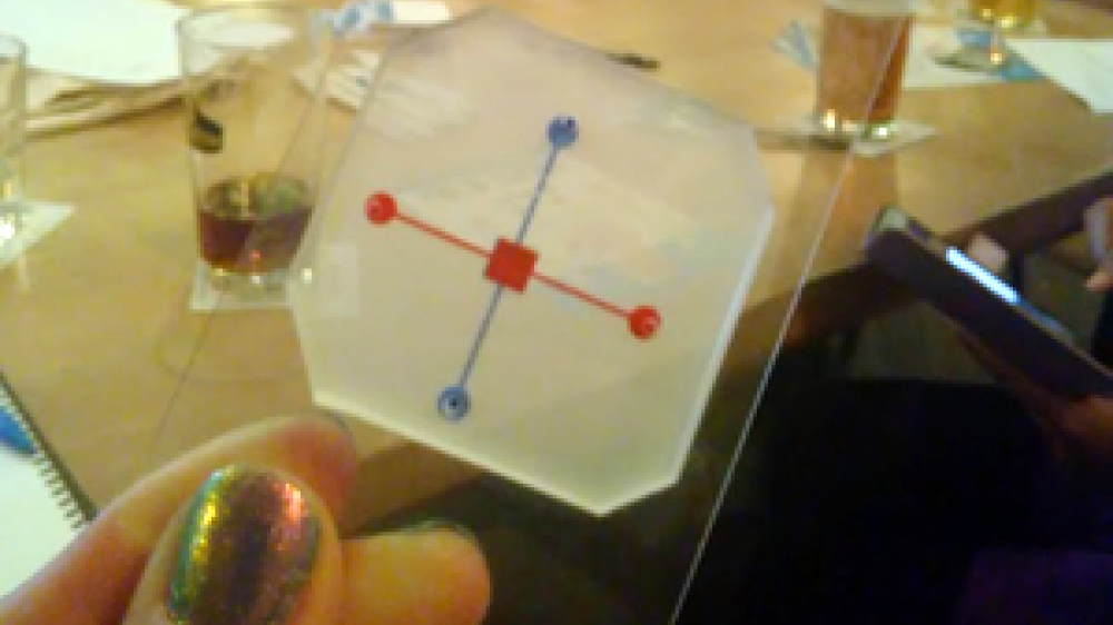 A person holding a Organs-on-chips device. It has a red horizontal line and a blue vertical line. In the center is a red square