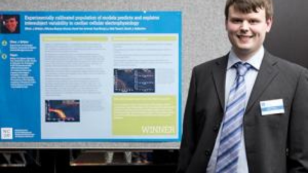 Dr Oliver Britton standing beside a 2014 winner poster for the international 3Rs prize