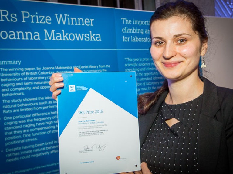 2016 Prize winner: Dr Joanna Makowska. Joanna is seen in front of a poster describing her work. She is holding up her prize certificate.