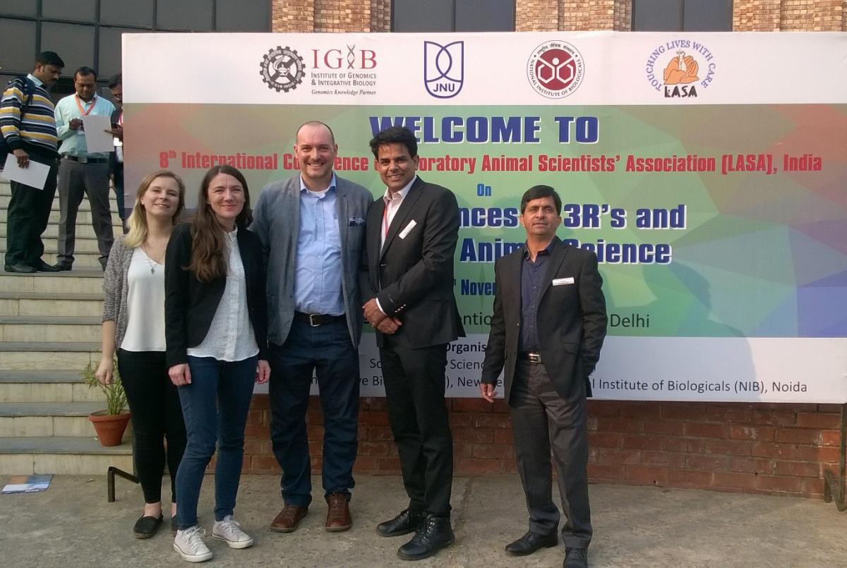 Dr Mark Prescott with four colleagues standing in front of the poster for the 8th annual conference of LASA India
