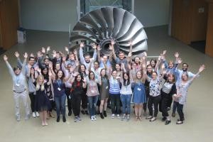 Students with there hands in the air standing in front of a large turbine 